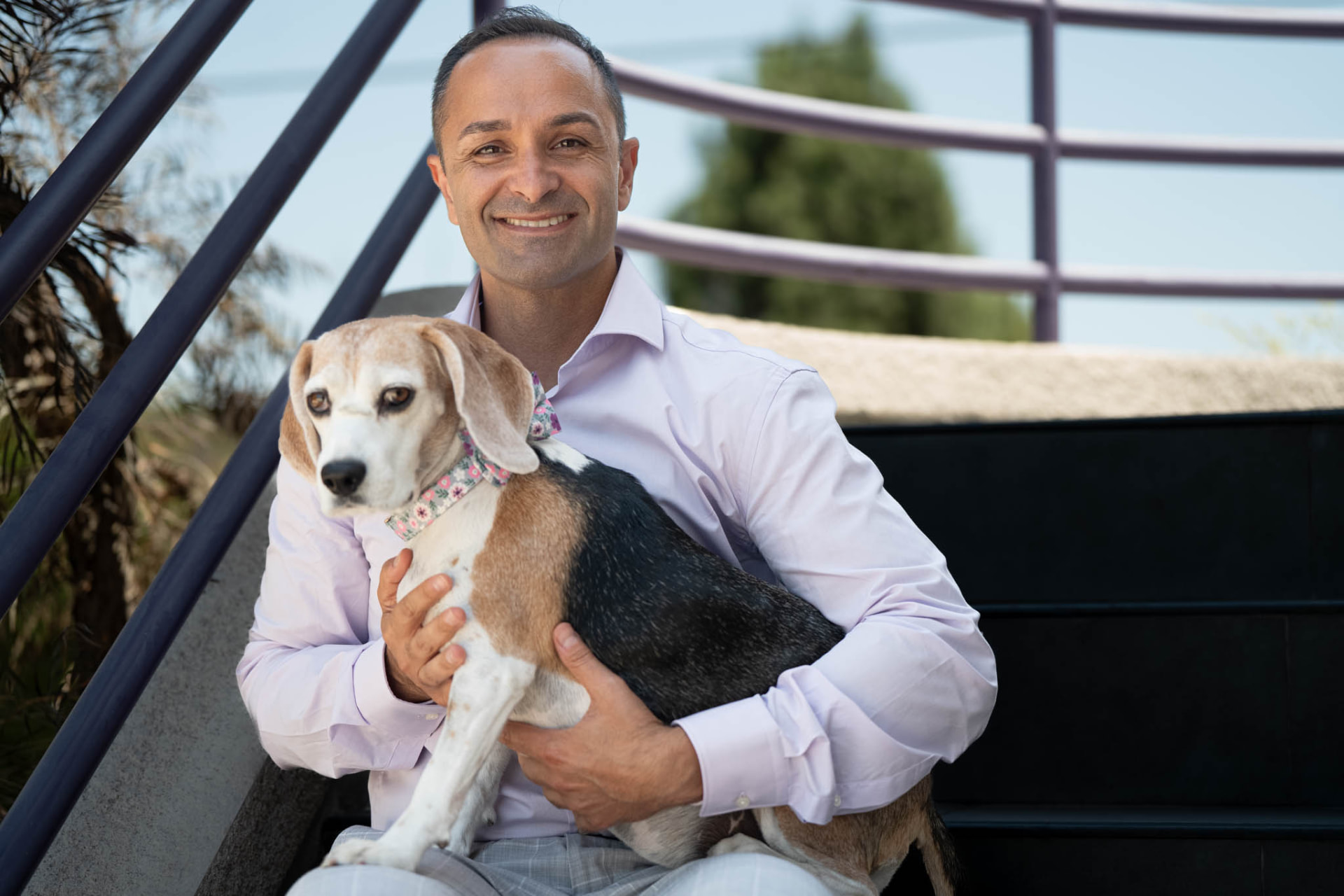Dr. Edmond Ahdoot smiling while holding his beagle on the office stairs
